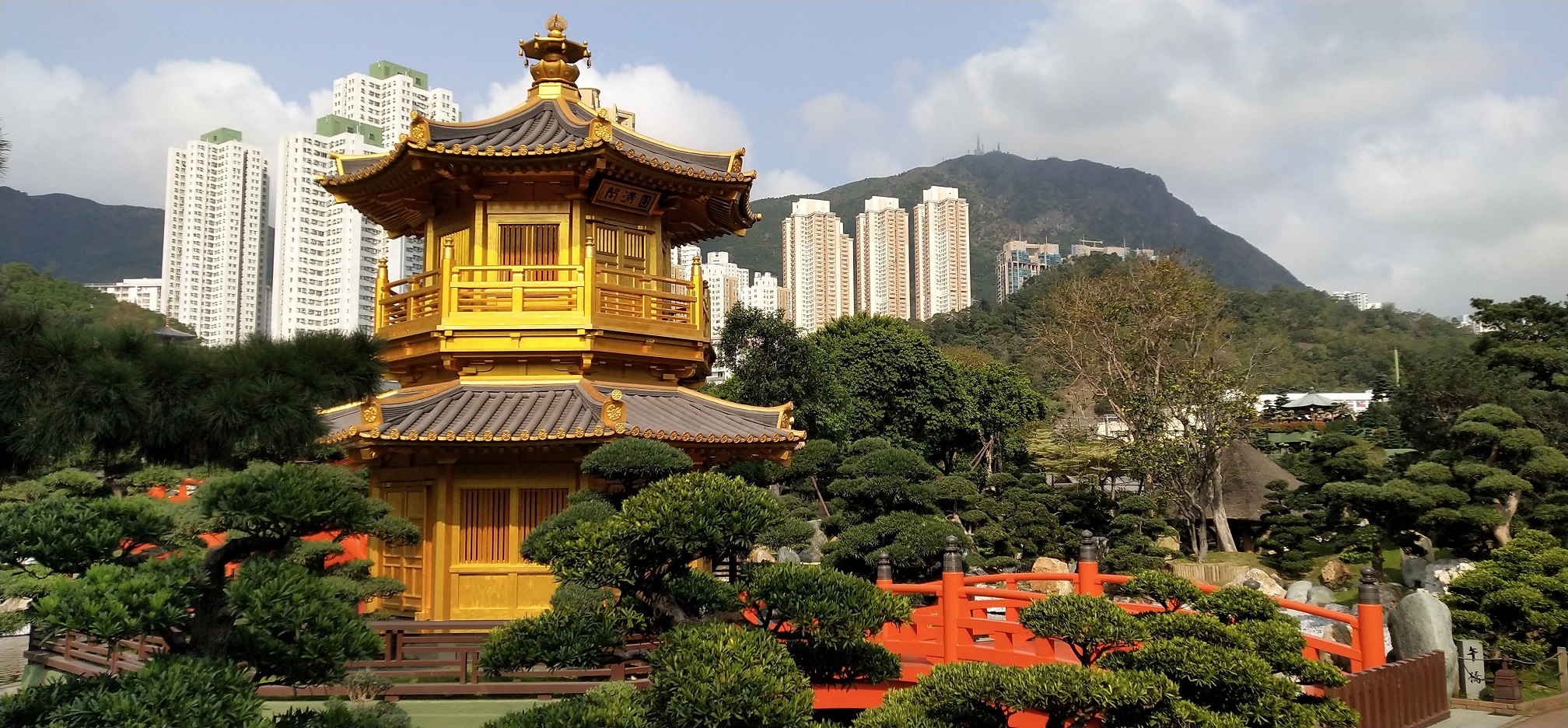 golden pavilion, red wooden bridge, trees, rocks, high rise buildings, blue sky, white cloud