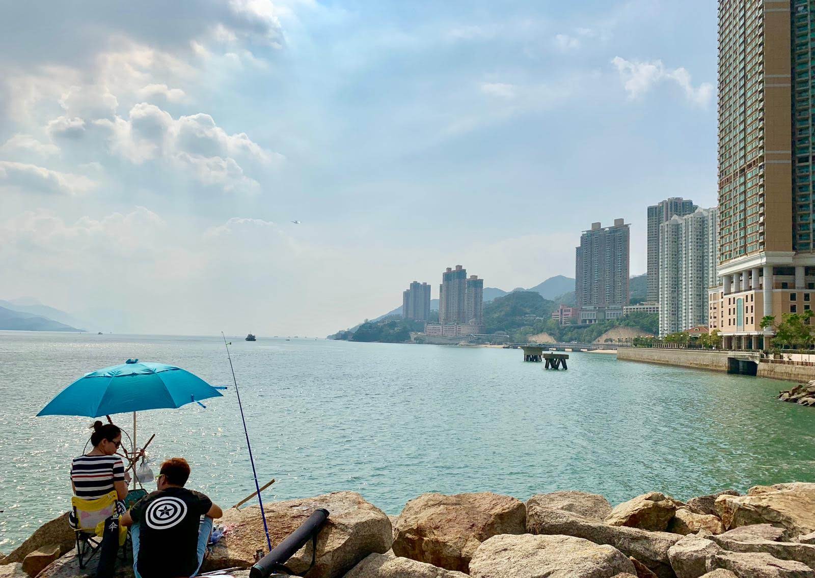 anglers under unbrella, sea, buildings on shoreline